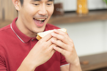 Asian smiling young man with casual  red t-shirt enyoy having breakfast, eating sandwich, Young man cooking food and drink in the loft style kitchen room