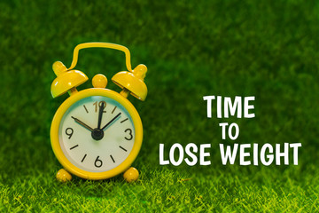yellow alarm clock on the grass background with the inscription 
