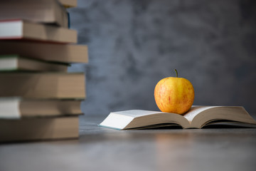 Jabłko leżące na otwartej ksiązce obok stosu lektur na tle betonu - obrazy, fototapety, plakaty