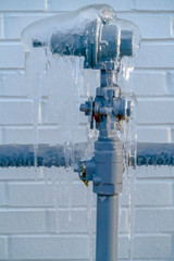 Close up of a gray metal pipe covered ice with against a white brick wall