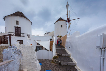 Tourists near windmill in the colorful village of Oia on a rainy day