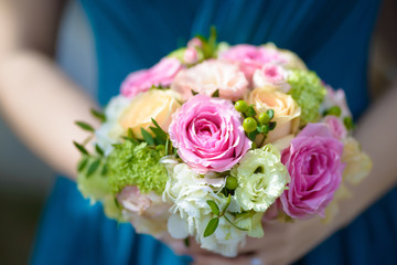 Obraz na płótnie Canvas Bridesmaid dressed in a blue dress holding a round colorful wedding bouquet featuring fresh pink roses, wild flowers and greenery traditional floral arrangement for female members of the bride's party