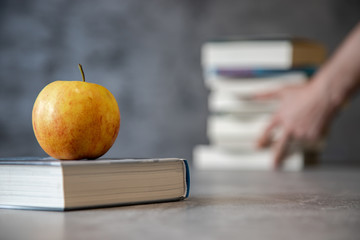 Jabłko leżące na książce, a w tle ręce trzymające stos książek - obrazy, fototapety, plakaty
