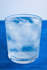  Transparent glass with water and ice cubes on a blue background