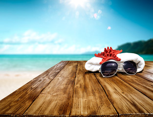 Desk of wood and free space for your decoration. White towel on top with sunglasses and red shell. Free space for your product and landscape of ocean with small island. 