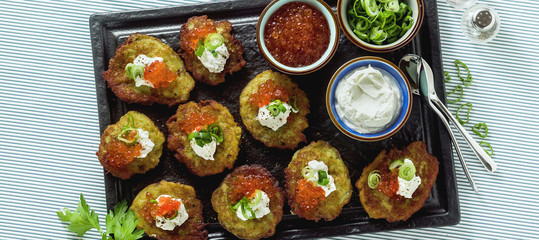 banner of Russian traditional potato pancakes served with red caviar, green onions and sour cream on a tray with white wine and lemon