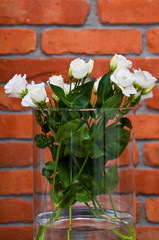 White eustoma flowers in glass on red brick wall background