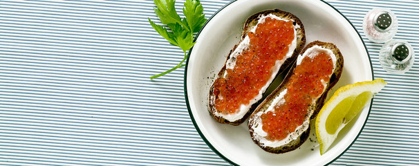 banner of Fresh bread sandwich with red caviar and soft cheese on a plate. classic combination of ingredients. snack on the table