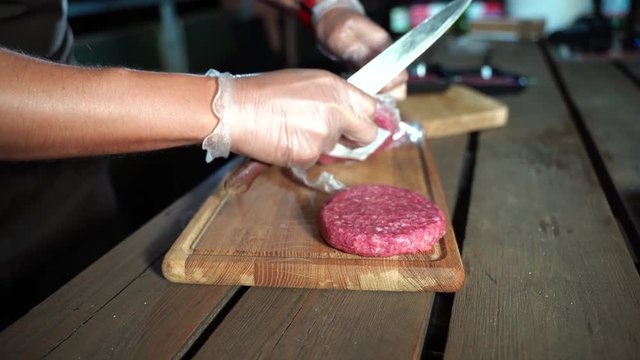 Raw hamburgers packed in food pellicle. Man opening burgers with knife