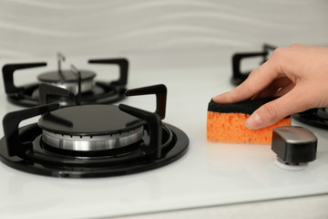 Fototapeta premium Woman cleaning gas stove with sponge, closeup