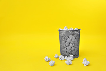 Metal bin with crumpled paper on color background, space for text