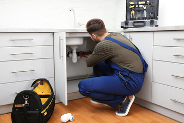 Male plumber in uniform repairing kitchen sink