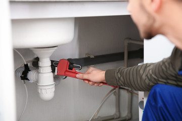 Male plumber repairing kitchen sink with pipe wrench, closeup