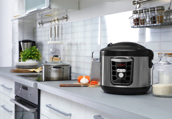 Modern multi cooker and products on table in kitchen. Space for text