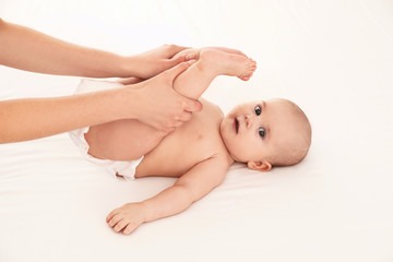 Mother and her cute child on white bed. Baby massage and exercises