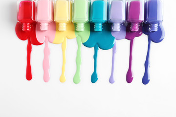 Spilled colorful nail polishes and bottles on white background, top view