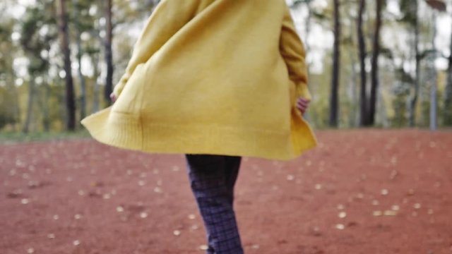 A young woman in a yellow sweater walks in the autumn park. legs and sweater closeup. woman dancing in the autumn park close-up.