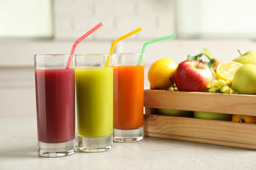 Three glasses of juices next to wooden crate with fresh ingredients on light table