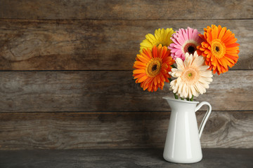 Bouquet of beautiful bright gerbera flowers in vase on table against wooden background. Space for text