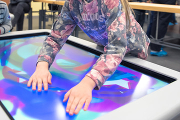 The hand of the child stretches to press the icon on the touchscreen of the interactive table