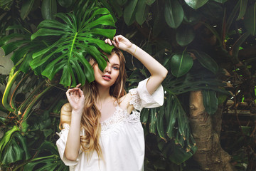 Young beautiful happy blonde girl model on tropical plants background with green leaf