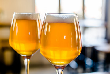      Two glasses of beer are on the bar table.