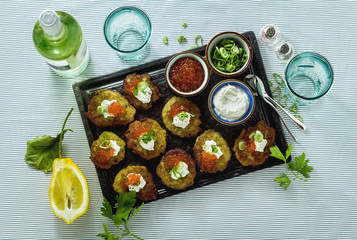 Russian traditional potato pancakes served with red caviar, green onions and sour cream on a tray with white wine and lemon