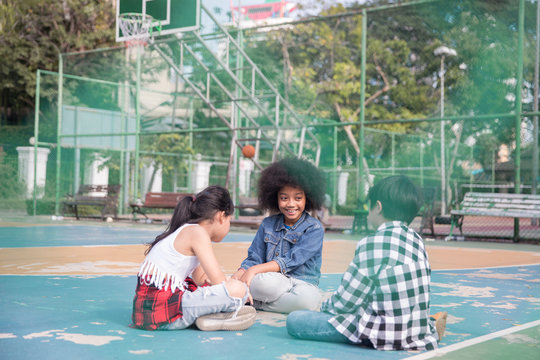 Group of kids sitting on a basketball court in a park