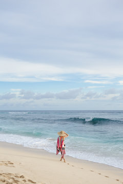 Back view: woman in swimwear walk on the beach