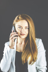 Junge Frau mit Jeans und weißem Blazer lächelt und hält Ihr Smartphone in der Hand, telefoniert...