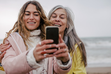 Senior woman and her daughter taking a selfie on the beach.