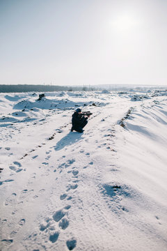 Unrecognizable man sitting on the snowy road by the sunny winter landscape with gun