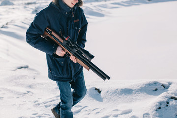 Unrecognizable man walking by the snow with rifle