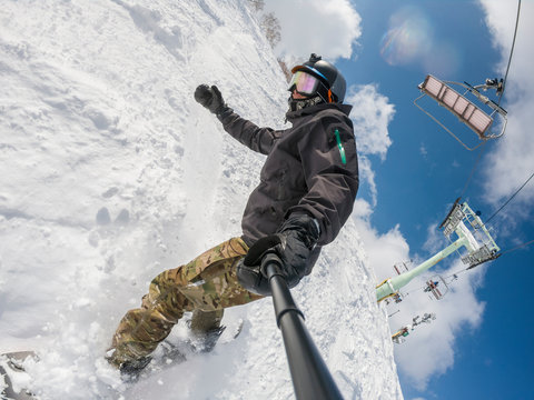 A snowboarder with action cam taking selfie on a ski slope at the Niseko