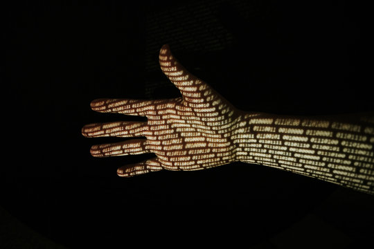 Hand in front of black background with binary code projected onto the skin.