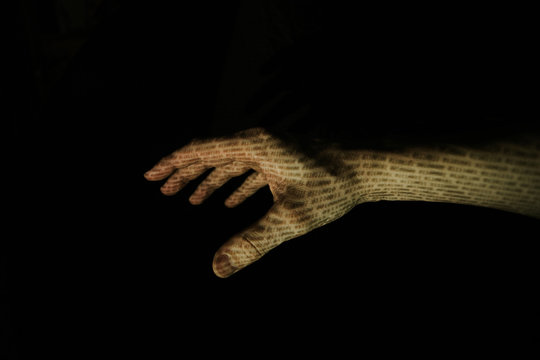 Hand in front of black background with binary code projected onto the skin.