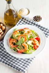 Fresh shrimp salad made of tomato, ruccola, avocado, prawns, chicken breast, arugula, crackers and spices. Caesar salad in a white, transparent bowl on wooden background