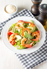 Fresh shrimp salad made of tomato, ruccola, avocado, prawns, chicken breast, arugula, crackers and spices. Caesar salad in a white, transparent bowl on wooden background