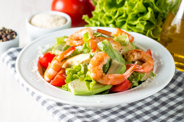 Fresh shrimp salad made of tomato, ruccola, avocado, prawns, chicken breast, arugula, crackers and spices. Caesar salad in a white, transparent bowl on wooden background