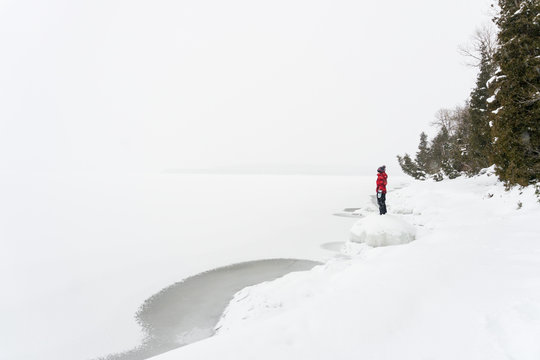 Solitary boy stands at edge of frozen lake