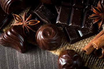 Assortment of dark, white and milk chocolate stack, chips. Chocolate and coffee beans on rustic wooden sacking background. Spices, cinnamon. Selective macro focus. Chocolates background. Sweets
