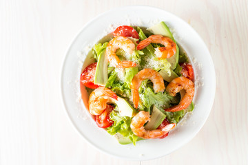 Fresh shrimp salad made of tomato, ruccola, avocado, prawns, chicken breast, arugula, crackers and spices. Caesar salad in a white, transparent bowl on wooden background