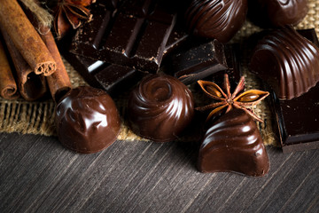 Assortment of dark, white and milk chocolate stack, chips. Chocolate and coffee beans on rustic wooden sacking background. Spices, cinnamon. Selective macro focus. Chocolates background. Sweets