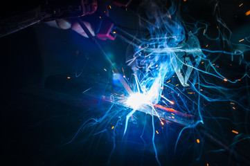 Worker with protective gloves welding metal part in workshop