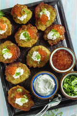 Russian traditional potato pancakes served with red caviar, green onions and sour cream on a tray with white wine and lemon