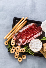 cold cuts and cheese are served on a tray on a table with white wine, crackers, grissini and taralli with aromatic herbs on a blue linen festive tablecloth.