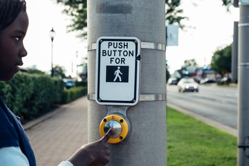 Black girl pushing the button of a crossing street light