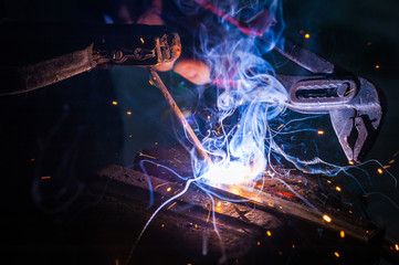 Worker with protective gloves welding metal part in workshop