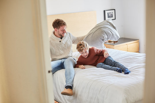 Dad And Son Playing A Pillow War On A Bed At Home