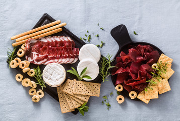 cold cuts and cheese are served on a tray on a table with white wine, crackers, grissini and taralli with aromatic herbs on a blue linen festive tablecloth.